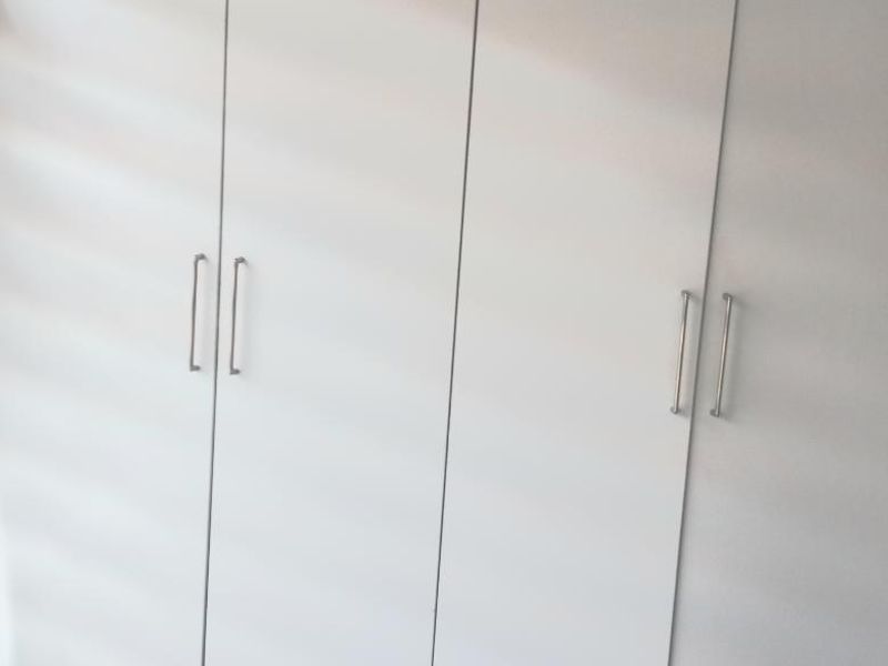 A close-up view of modern, white built-in bedroom cupboards with sleek metal handles.