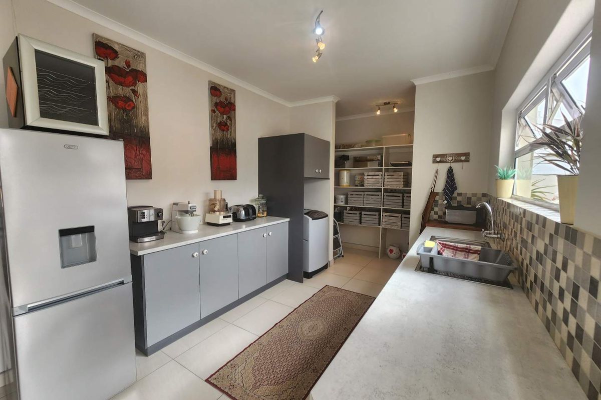 A functional kitchen and scullery area featuring grey cabinetry, light countertops, tiled flooring, and a dedicated pantry storage section.