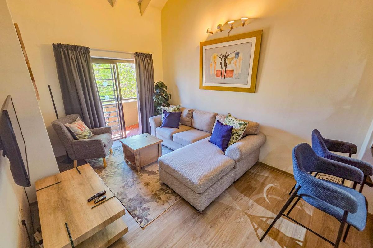 A bright living room featuring vaulted ceilings, laminate flooring, and a sliding glass door providing access to an outdoor balcony area.