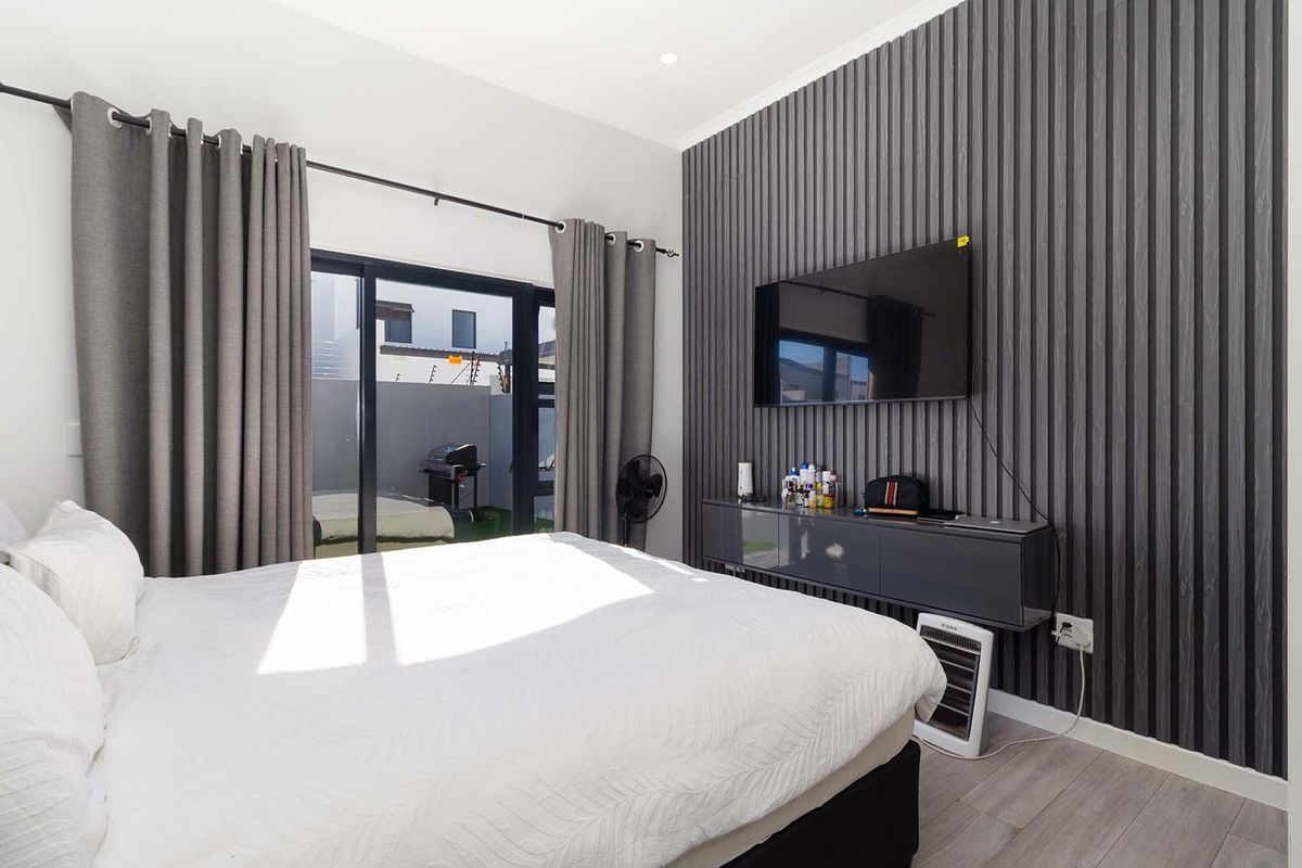 Modern bedroom featuring a textured charcoal feature wall, laminate flooring, and sliding glass doors providing direct access to the rear patio area.