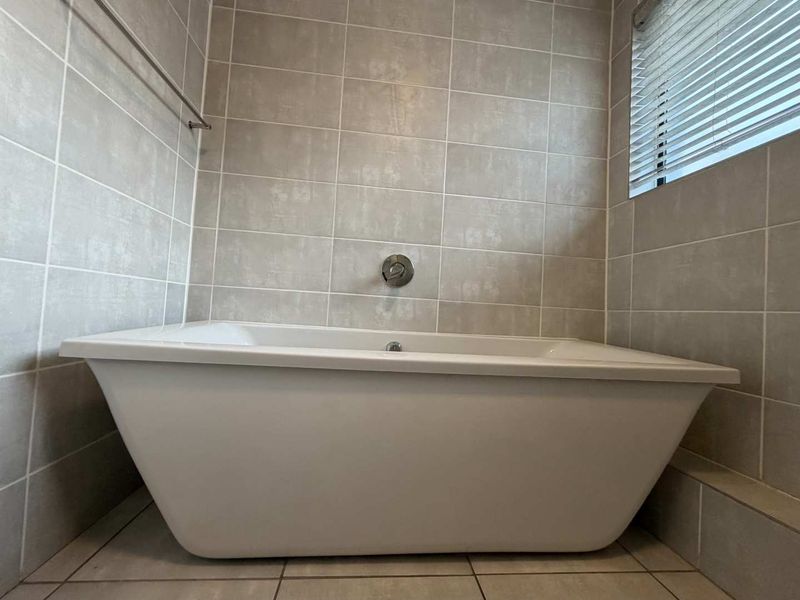 A clean, modern bathroom featuring a white freestanding bathtub, neutral wall tiling, and a functional wall-mounted mixer tap.