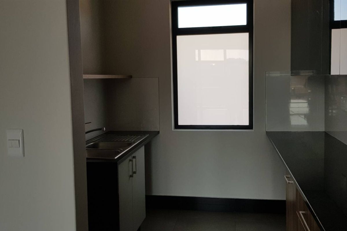 A clean, modern scullery featuring dark granite countertops, built-in cabinetry, and a stainless steel sink, providing a functional secondary prep and wash-up area.