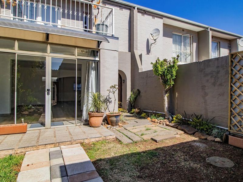 Rear exterior view of the townhouse featuring a paved patio area, small garden space, and an upper-level balcony with wrought iron railings.