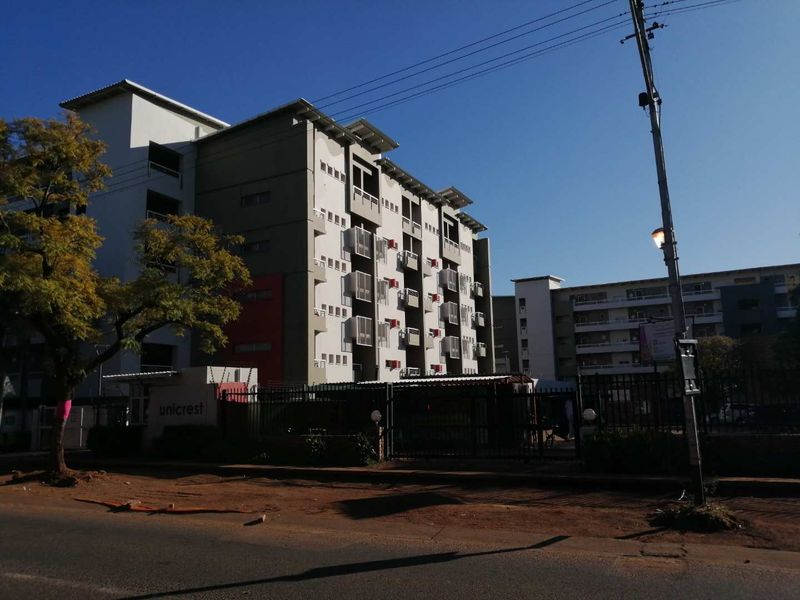 Street view of the Unicrest apartment complex, featuring a multi-story building with balconies and secure gated access.