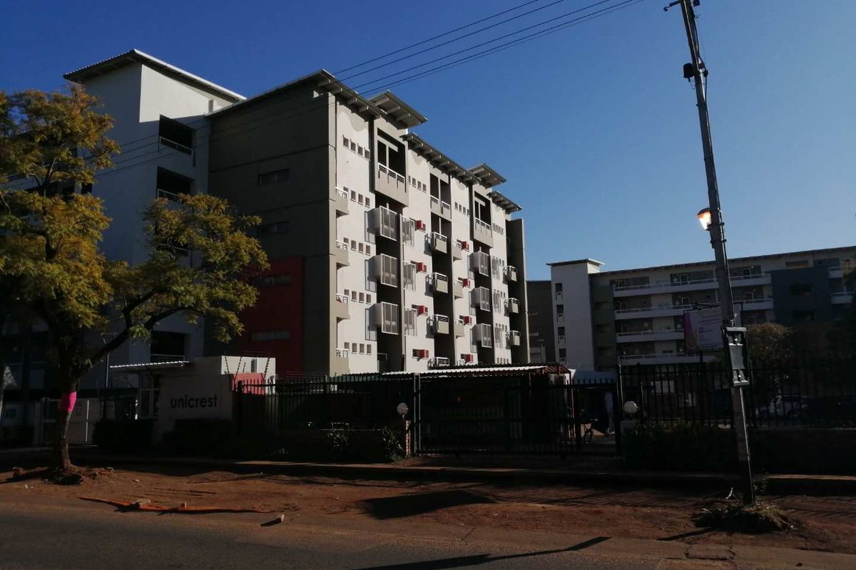 Street view of the Unicrest apartment complex, featuring a multi-story building with balconies and secure gated access.