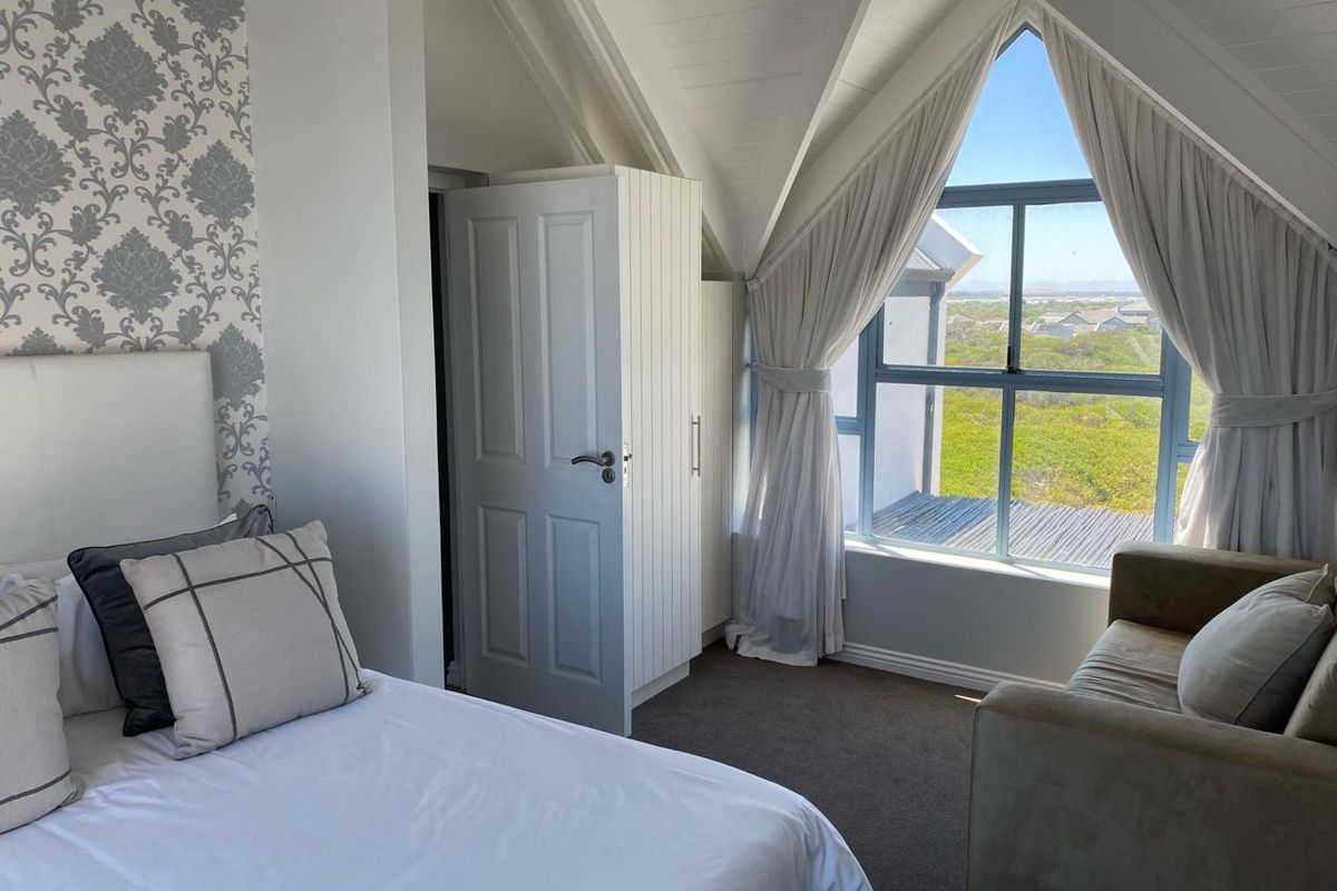 A bright bedroom featuring a vaulted ceiling, built-in wardrobe, and a large window offering scenic views of the surrounding landscape.