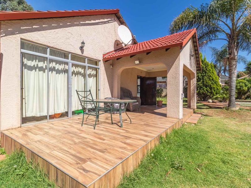 A covered patio area featuring wood-look tiled flooring, sliding glass doors, and direct access to the garden, providing a functional outdoor living space.