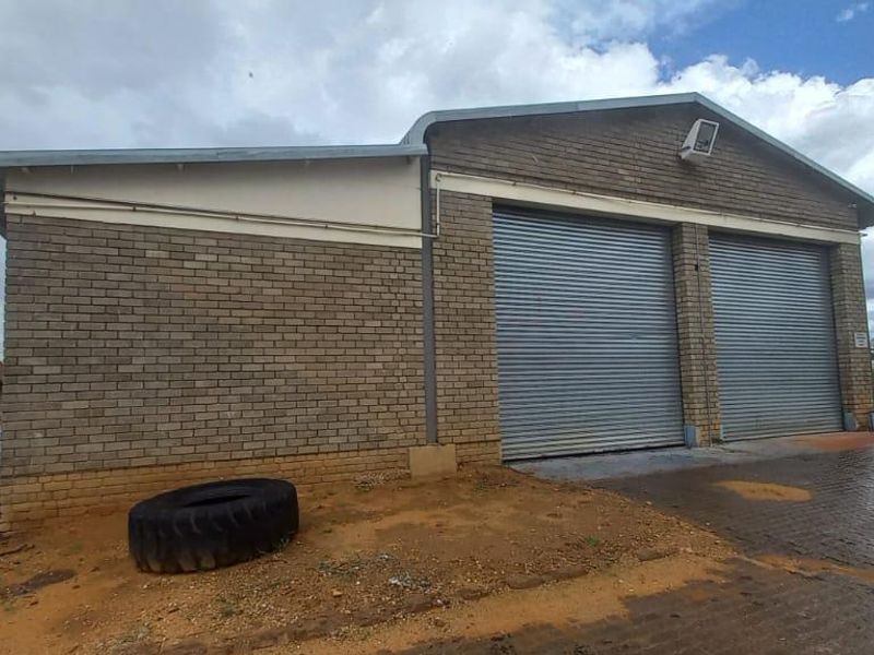 Industrial property featuring a brick facade with two secure roller shutter doors and a paved driveway area.