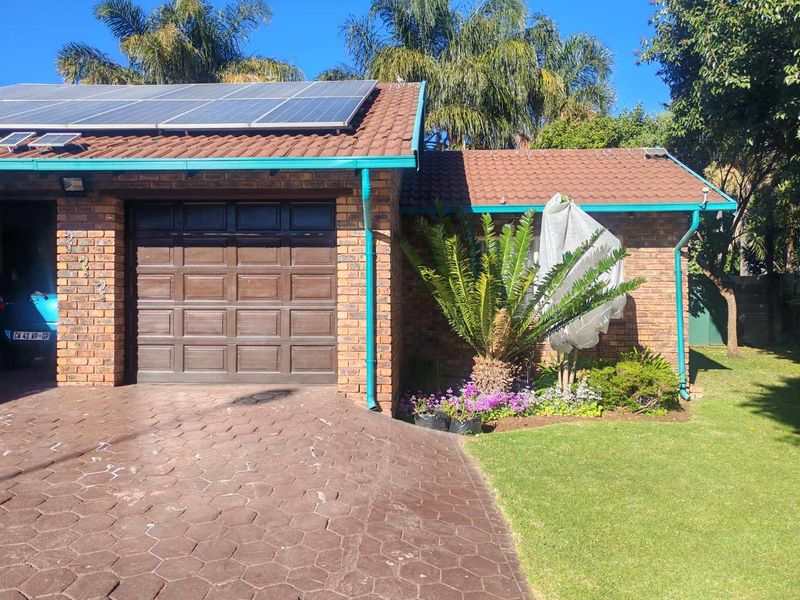 Front exterior view of the house featuring a brick facade, tiled roof with solar panels, a garage, and a paved driveway.