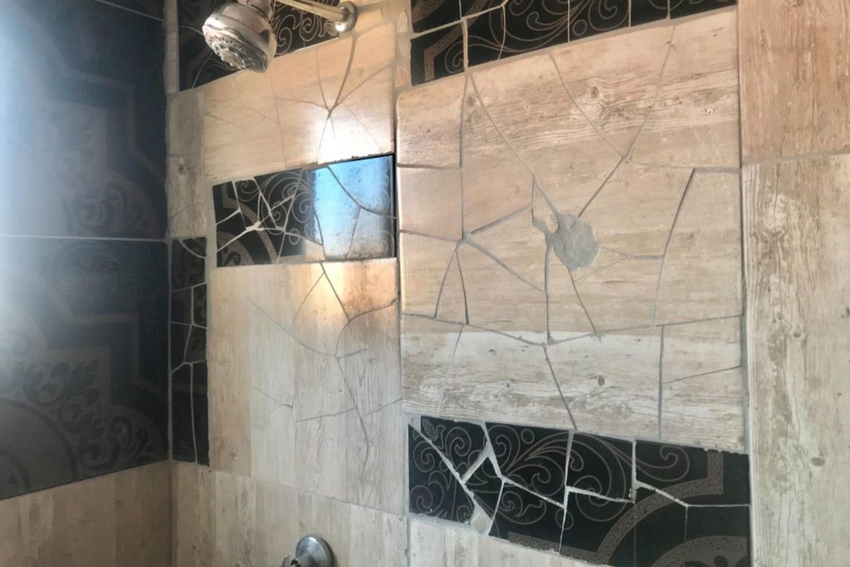 A shower enclosure featuring a mix of decorative and wood-look wall tiles with visible cracks and signs of poor installation.
