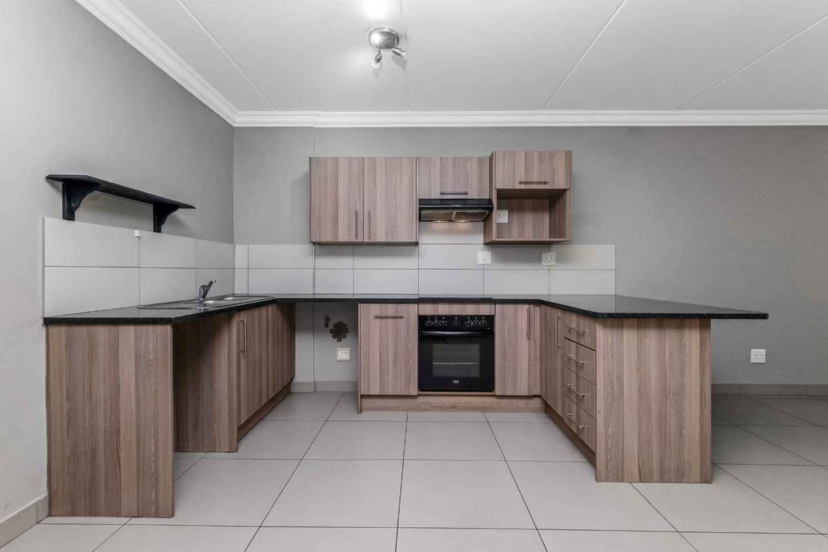 A functional kitchen featuring wood-look cabinetry, dark granite countertops, a built-in oven, extractor fan, and tiled flooring.