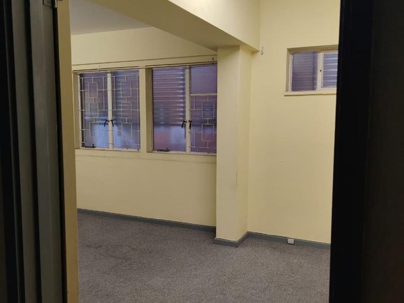 An empty, functional office space featuring carpeted flooring, security bars on the windows, and overhead fluorescent lighting.