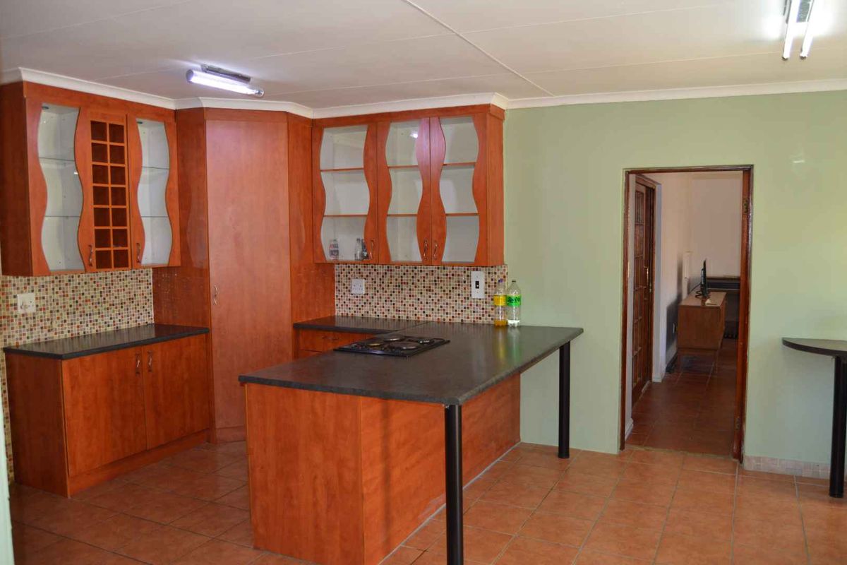 A functional kitchen featuring wooden cabinetry, a built-in gas hob, mosaic tile splashbacks, and tiled flooring with an open-plan layout.