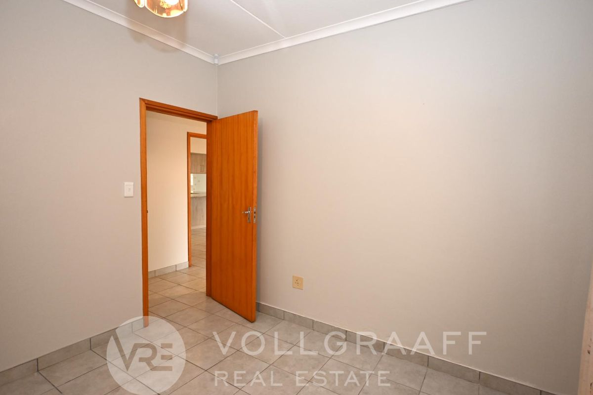 A clean, empty bedroom featuring neutral wall paint, tiled flooring, and a wooden door leading to an adjacent hallway.