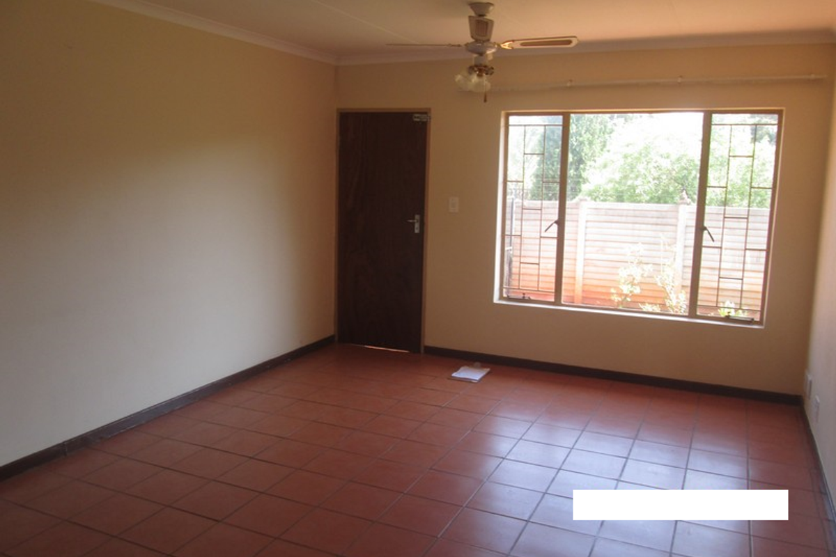 A spacious, empty living room featuring durable tiled flooring, a ceiling fan, and large windows with security bars, offering a blank canvas for personalization.
