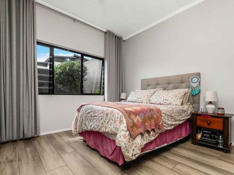 A well-maintained bedroom featuring modern laminate flooring, neutral wall tones, and large windows with floor-to-ceiling curtains providing ample natural light.
