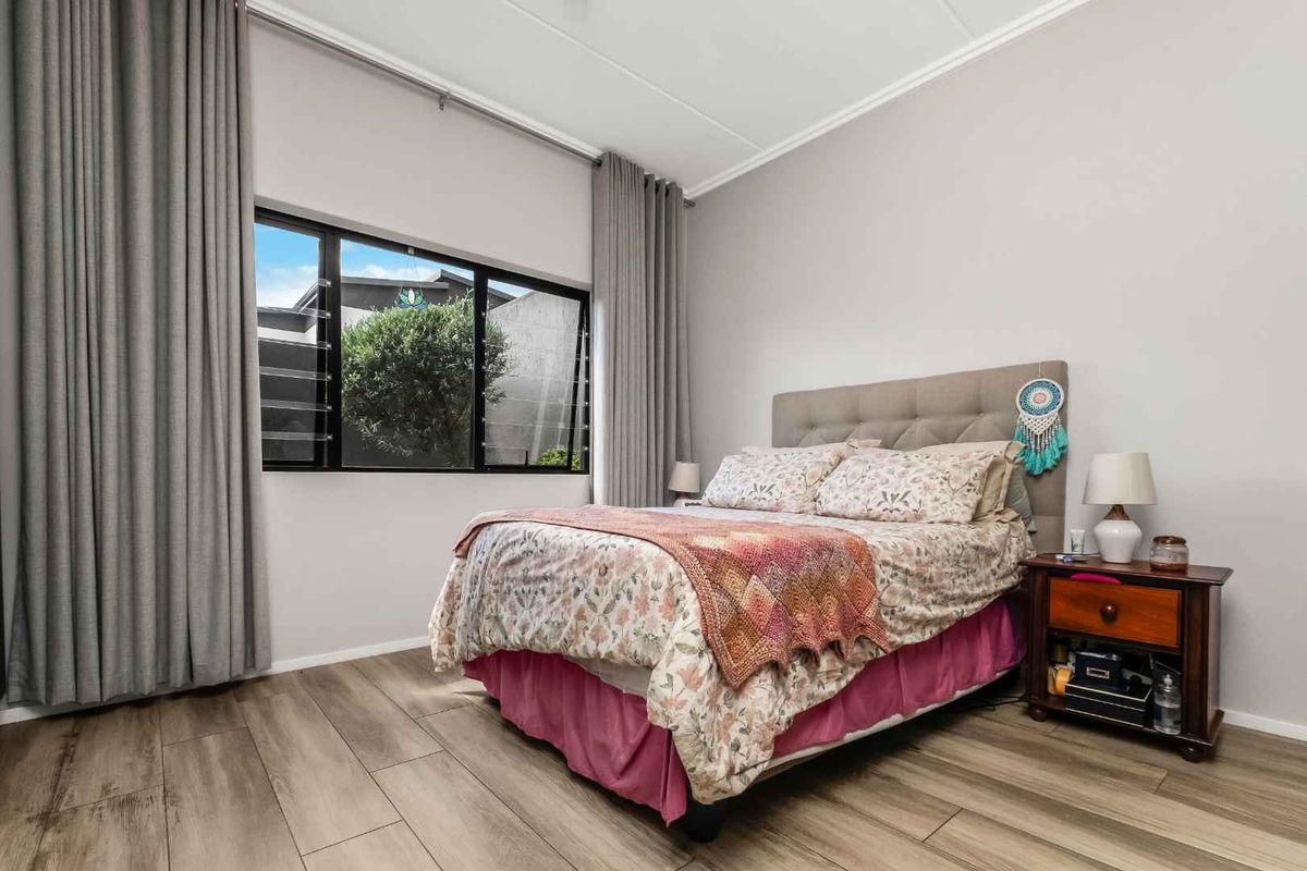 A well-maintained bedroom featuring modern laminate flooring, neutral wall tones, and large windows with floor-to-ceiling curtains providing ample natural light.