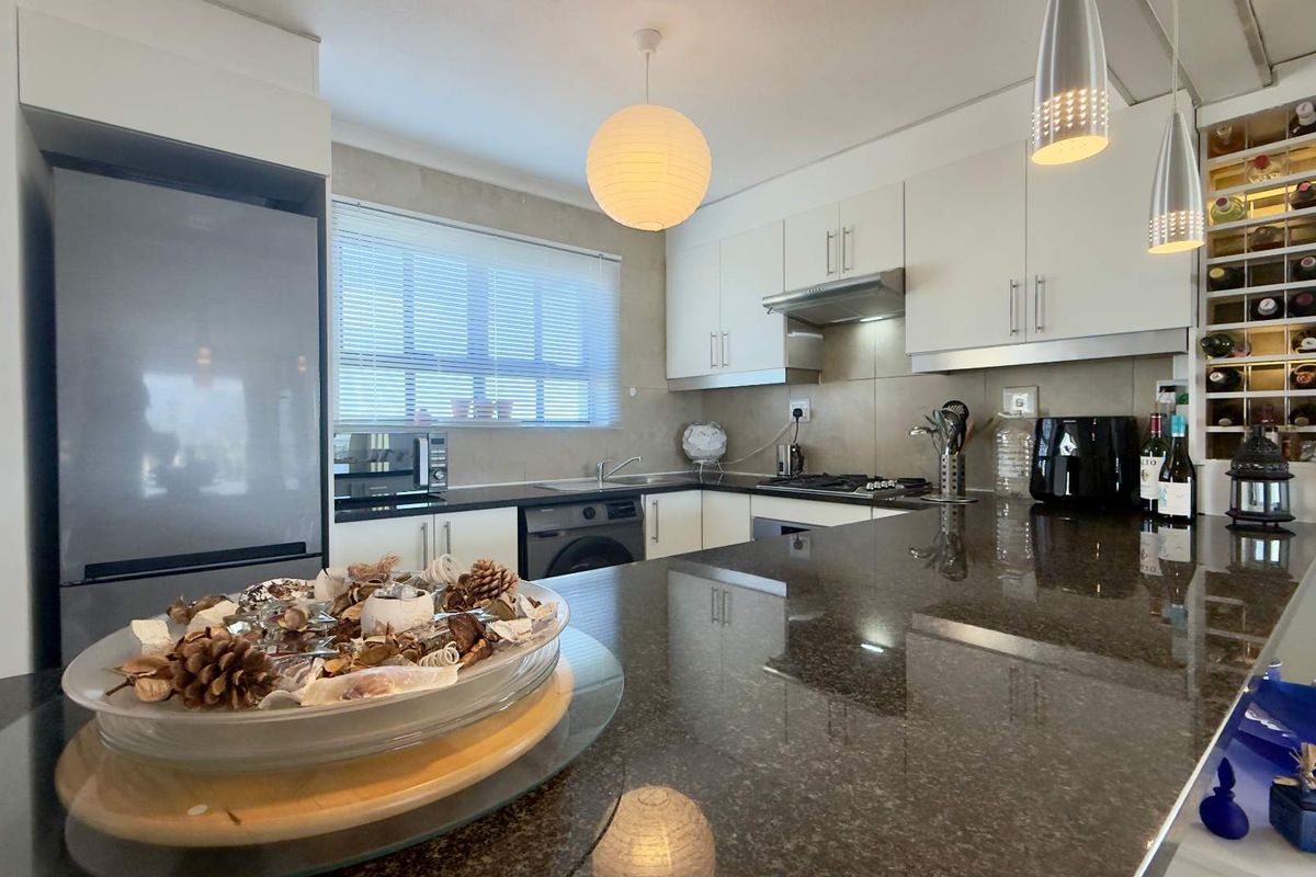 Modern kitchen featuring dark granite countertops, ample built-in cabinetry, a gas hob with extractor fan, and a dedicated built-in wine storage rack.