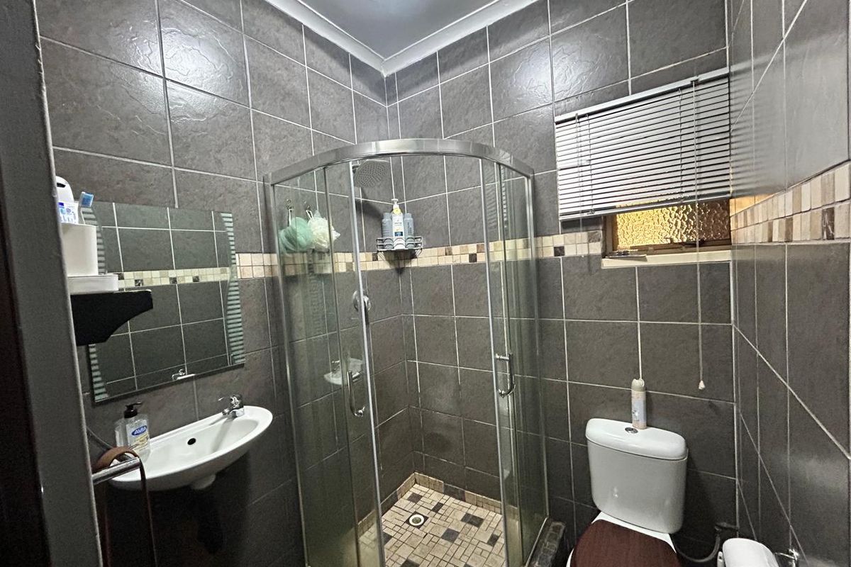 Compact bathroom featuring a corner glass shower enclosure, wall-mounted basin, and toilet, finished with dark grey wall tiles and mosaic accents.