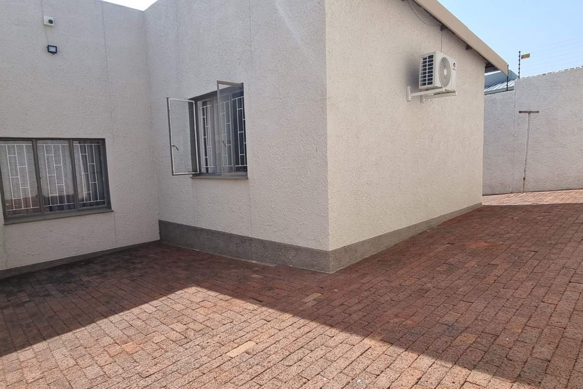 A private rear courtyard featuring brick paving, security-fitted windows, and an external air conditioning unit.
