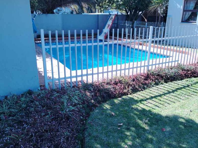 A private swimming pool area featuring a secure metal fence, paved surround, and established garden landscaping.