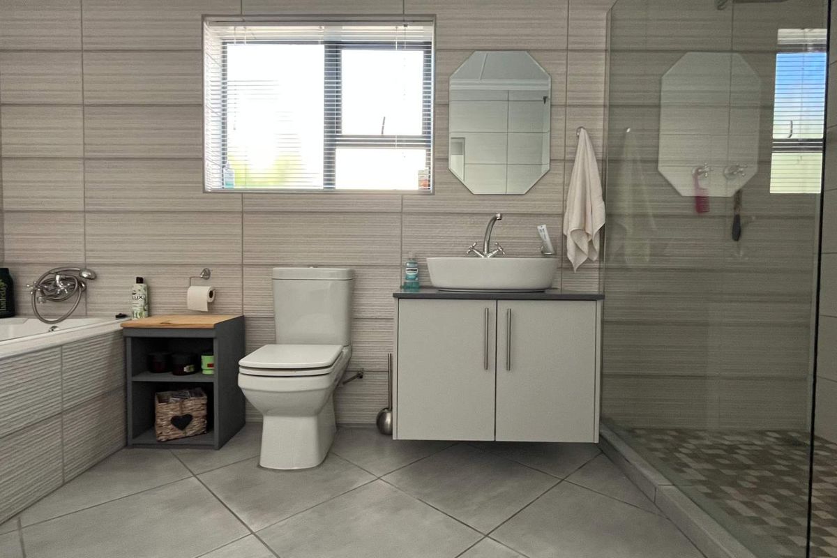 Modern bathroom featuring a floating vanity, vessel sink, glass-enclosed walk-in shower, and a built-in bathtub with neutral wall tiling.