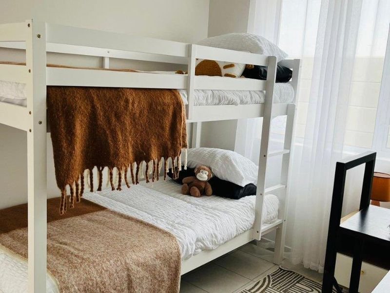A well-maintained bedroom featuring neutral wall tones, tiled flooring, and large windows with installed curtain rods.