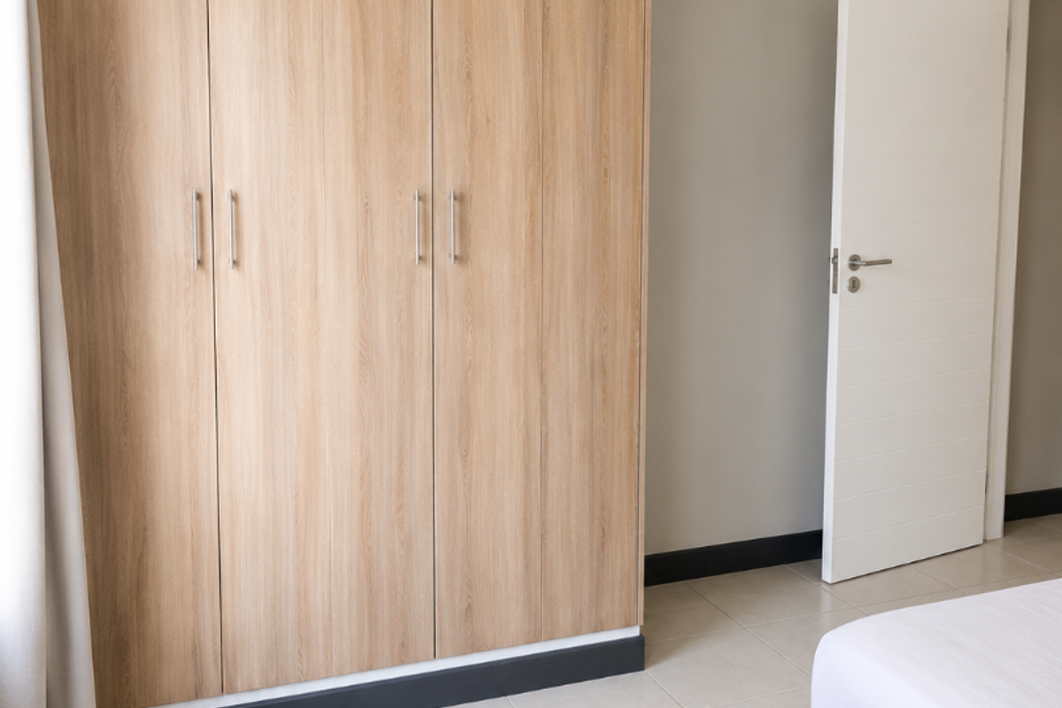A clean bedroom featuring light wood-finish built-in cupboards, neutral wall tones, and tiled flooring.