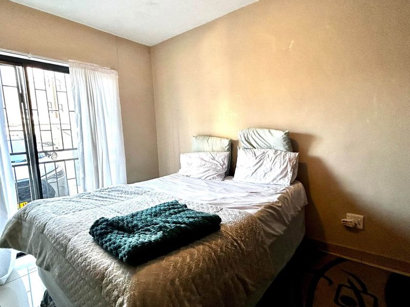 A bedroom featuring tiled flooring and a sliding glass door with security gate, showing signs of wear on the walls and ceiling.