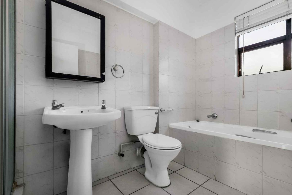 A functional bathroom featuring a pedestal sink, a standard toilet, and a built-in bathtub with full-height wall tiling.