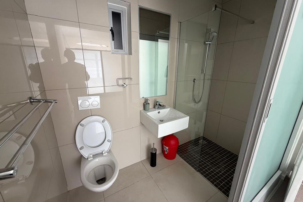 A modern, compact bathroom featuring a wall-mounted toilet, a wall-mounted basin, and a glass-enclosed shower with tiled finishes throughout.