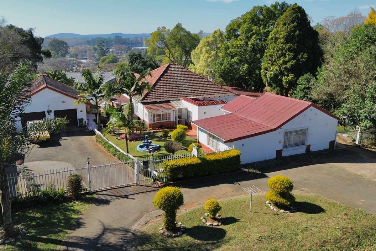 Aerial view of a residential property featuring a main house, detached garage, landscaped garden with a water fountain, and paved driveway access.