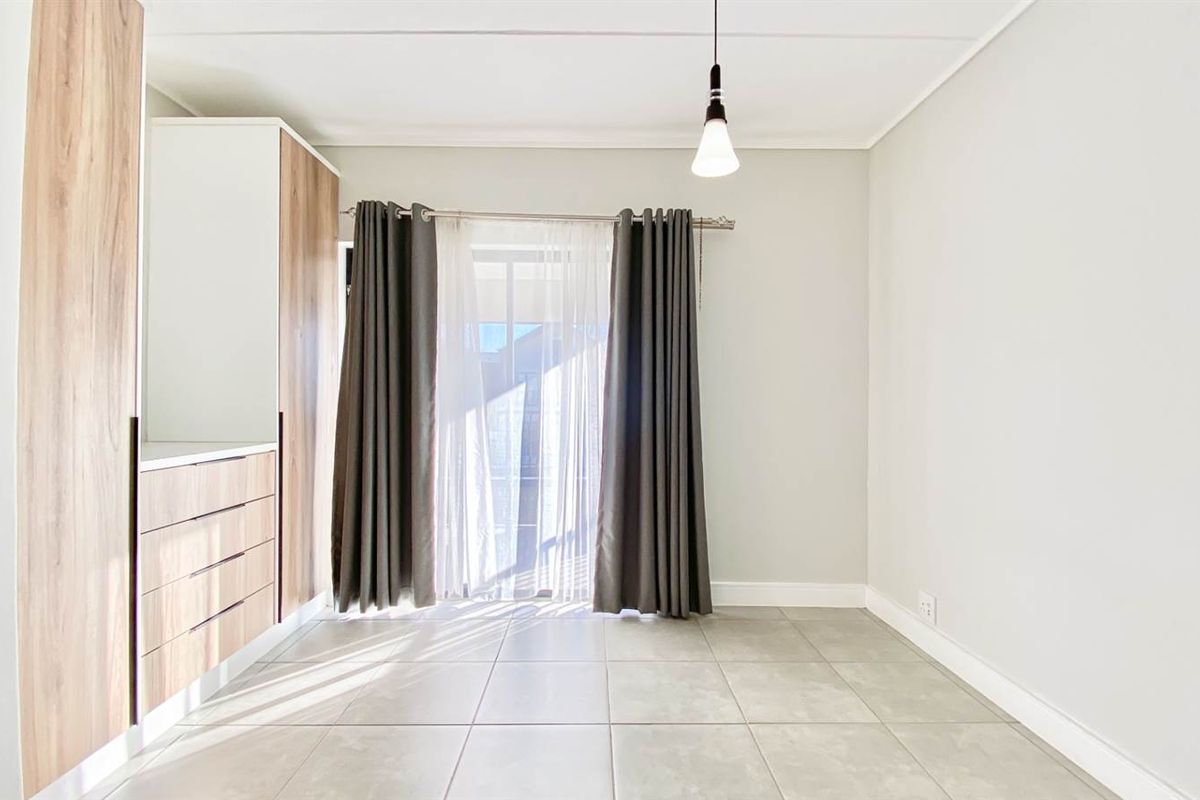 A bright, modern living area featuring neutral floor tiles, built-in cabinetry with wood-grain finish, and sliding glass doors leading to an outdoor space.
