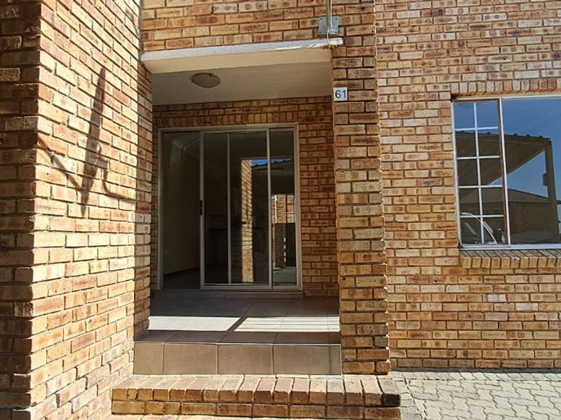 Front entrance of a townhouse featuring a face brick facade, tiled porch, and sliding glass door access.