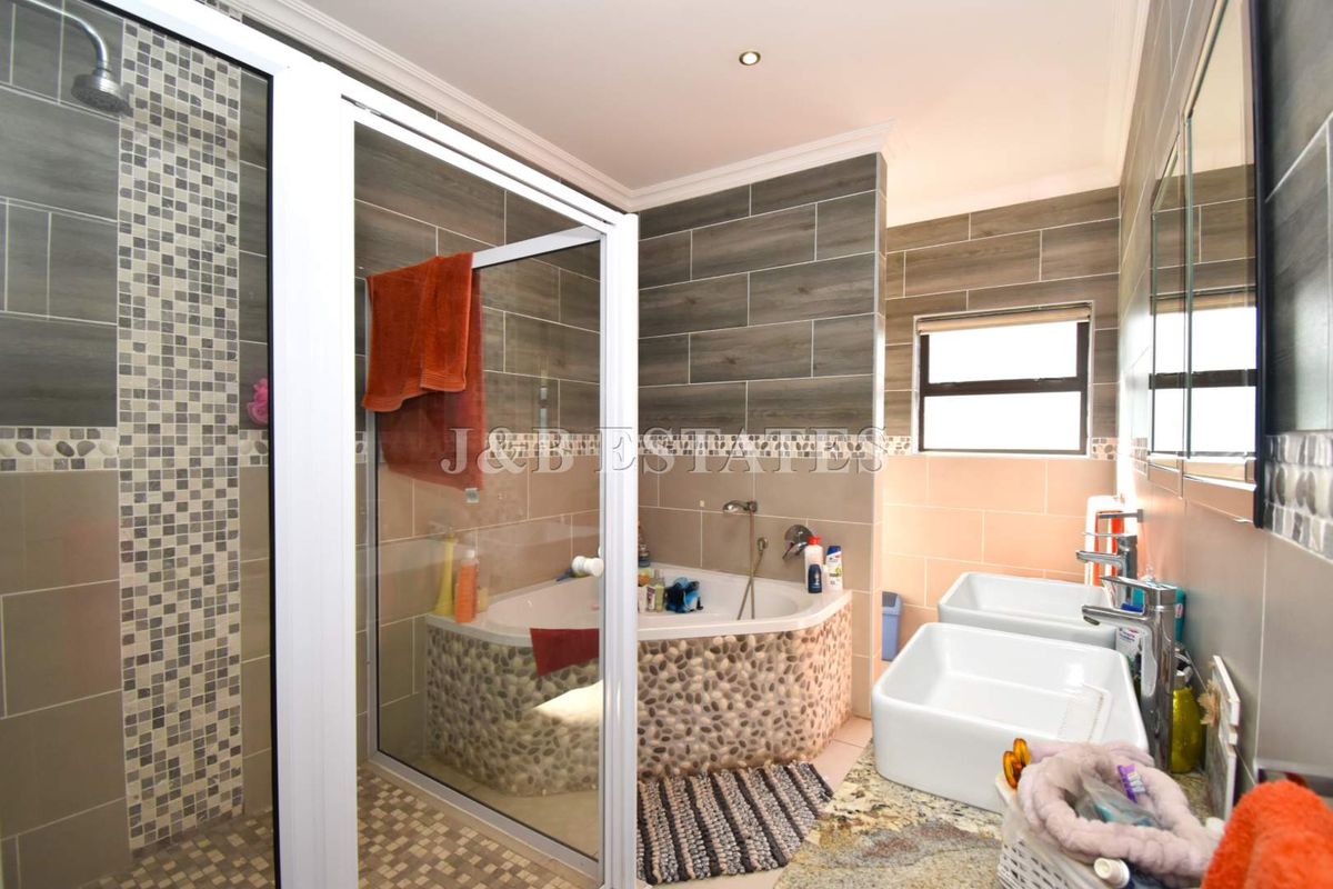 Modern bathroom featuring a corner bathtub with pebble-tiled surround, a separate glass-enclosed shower, and dual vessel sinks on a granite vanity top.