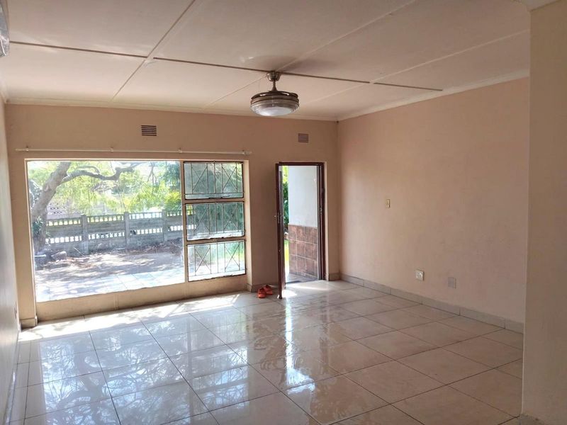 An empty living room featuring tiled flooring, a ceiling fan, and large windows providing natural light and access to the exterior.