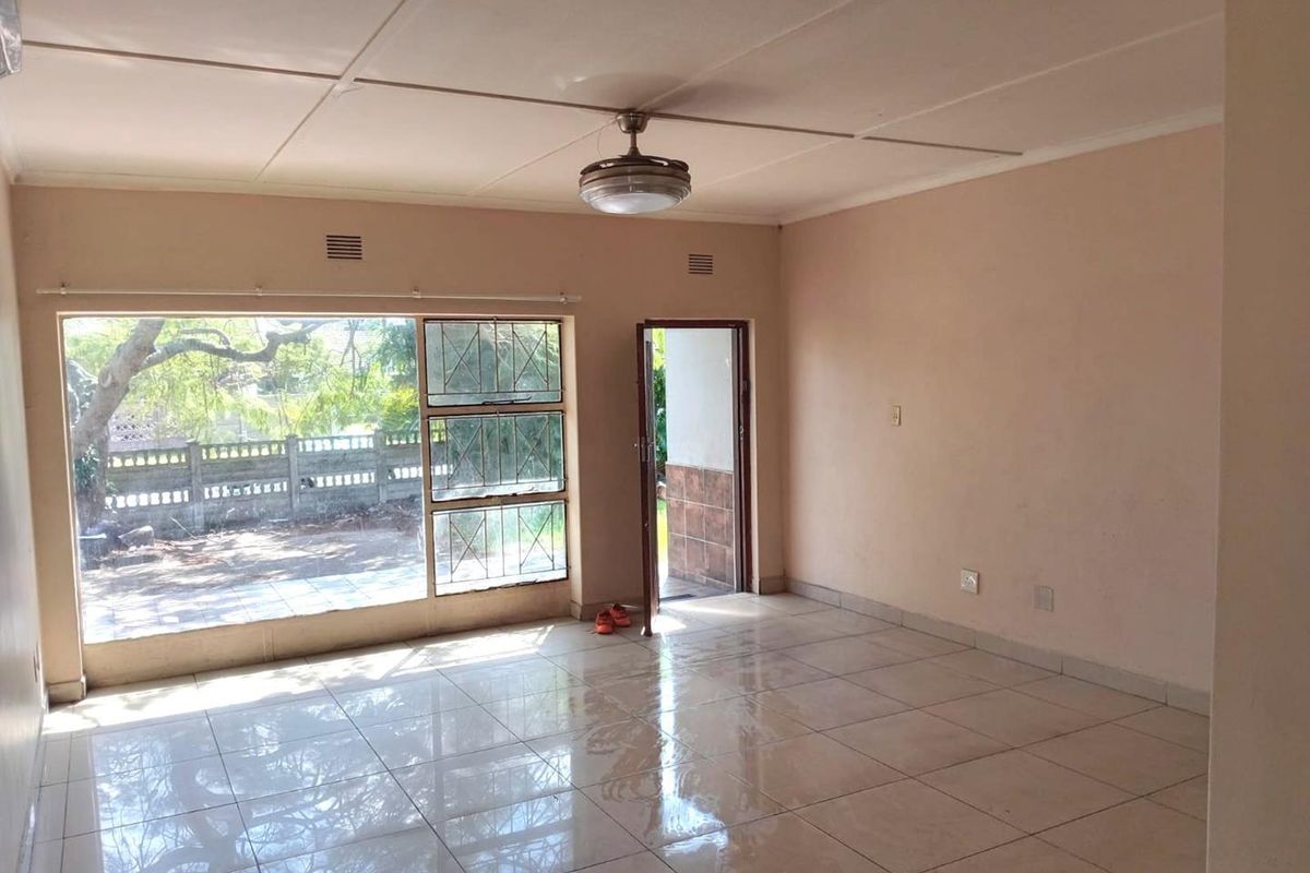An empty living room featuring tiled flooring, a ceiling fan, and large windows providing natural light and access to the exterior.