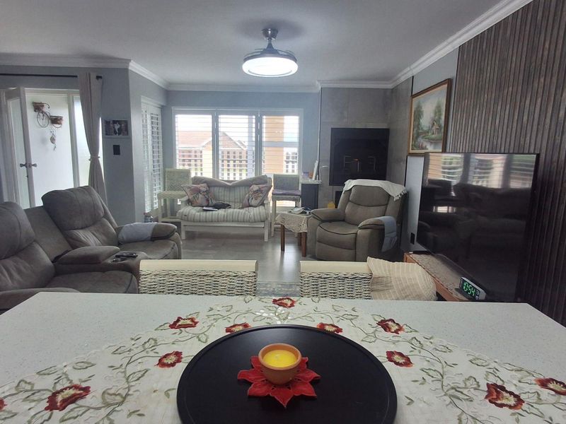 Spacious open-plan living area featuring a built-in fireplace, decorative wood paneling, and large windows providing ample natural light.