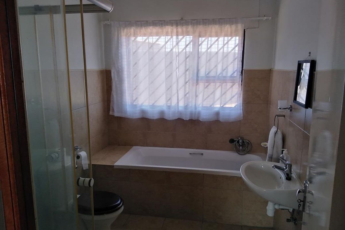 A functional bathroom featuring a built-in bathtub, pedestal washbasin, toilet, and a glass-enclosed shower with neutral wall and floor tiling.