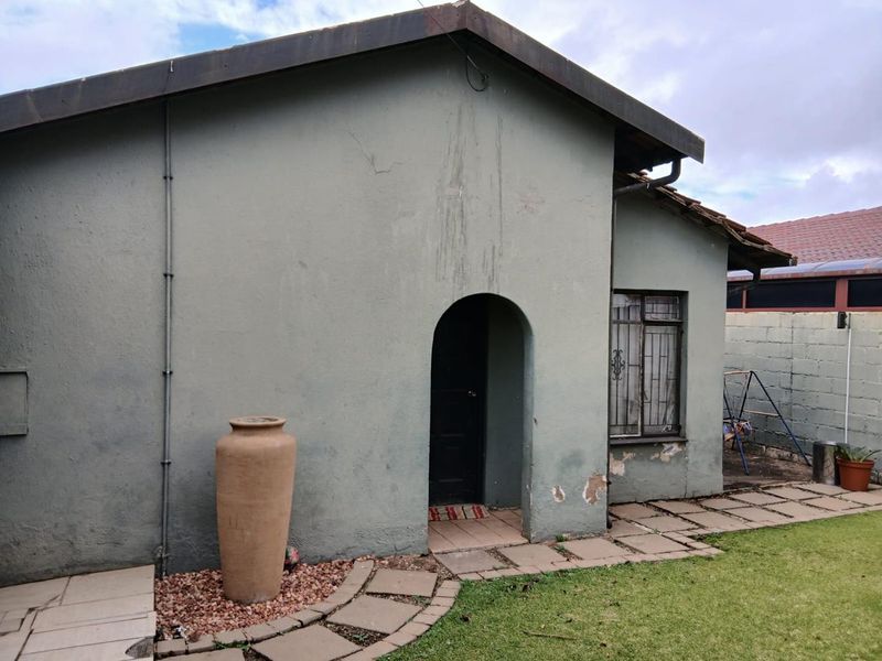 Rear exterior view of the house featuring an arched entrance, metal security bars on the window, and a paved walkway leading to the garden area.