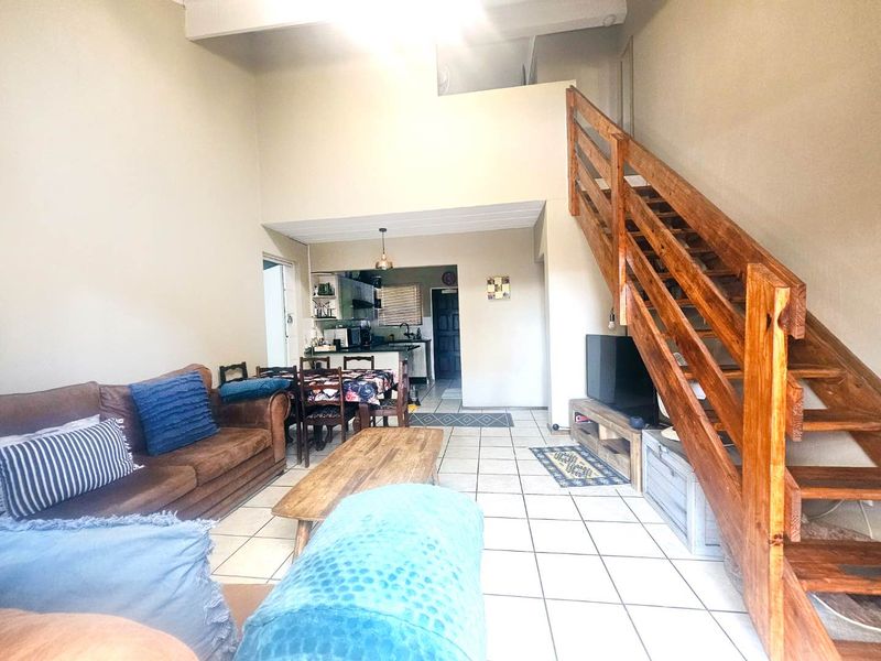 Open-plan living area featuring a double-volume ceiling, ceramic tiled flooring, and a prominent wooden staircase leading to the upper level.