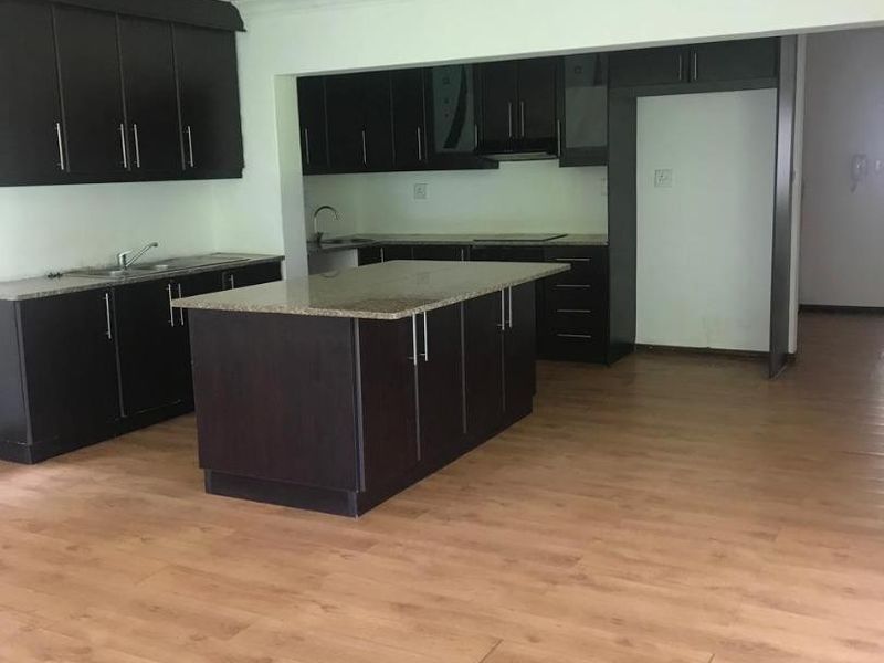 Spacious kitchen featuring dark cabinetry, granite countertops, a central island, and laminate flooring. The area is currently vacant and ready for personalization.