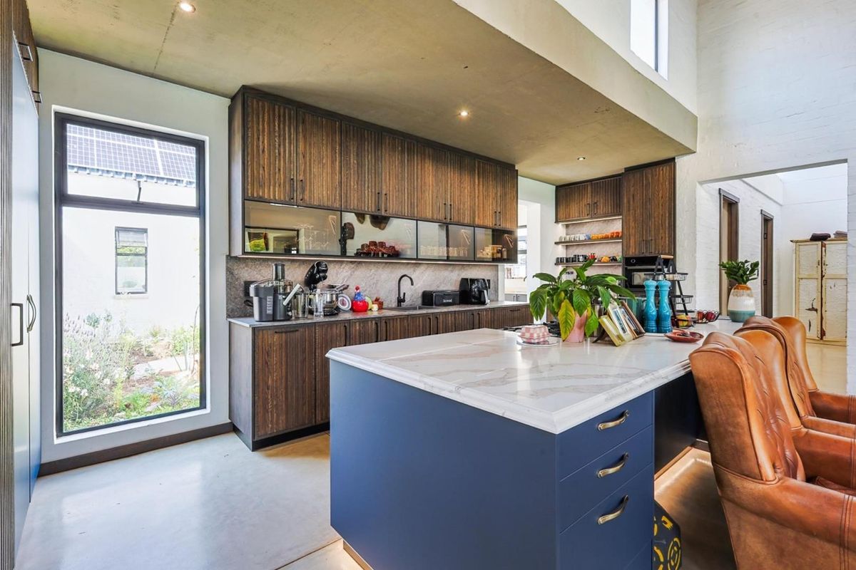 Modern kitchen featuring dark wood cabinetry, a large blue central island with stone countertop, and polished concrete flooring in an open-plan layout.