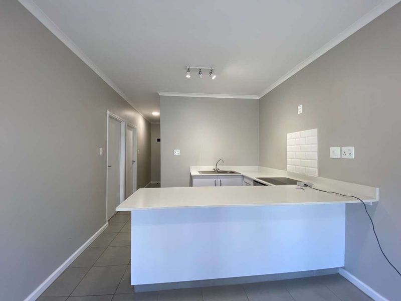 A clean, modern kitchen featuring a breakfast bar, built-in hob, subway tile splashback, and neutral grey walls with tiled flooring.