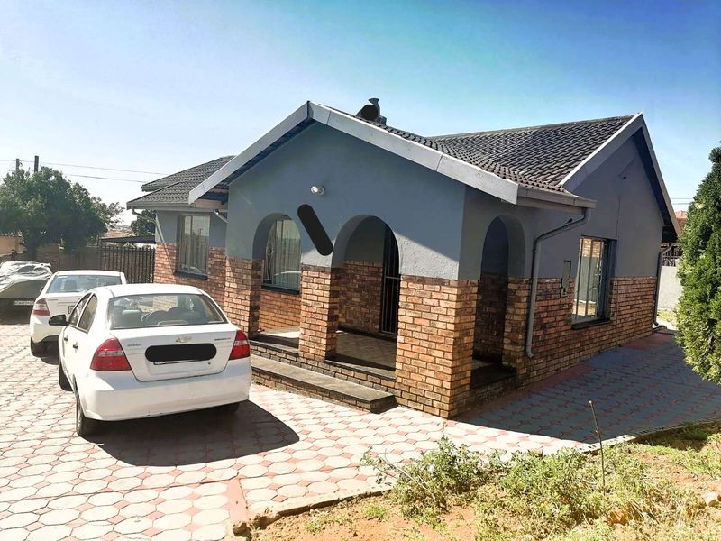 Front elevation of a single-story house featuring a brick and painted facade, tiled roof, and a paved driveway.