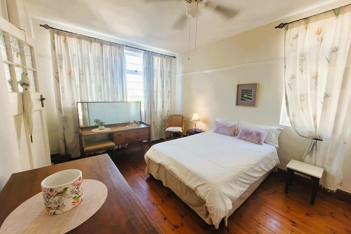 A well-lit bedroom featuring original timber flooring, a ceiling fan, and large windows with natural light.