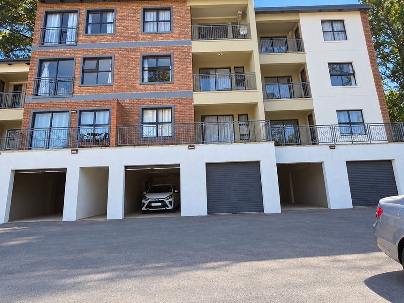Front elevation of a multi-story apartment building featuring brick and rendered facade, private balconies with metal railings, and ground-level covered parking bays.