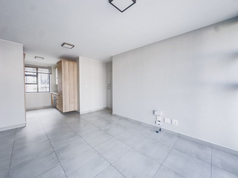 An open-plan living and kitchen area featuring neutral tiled flooring, modern built-in cabinetry, and integrated kitchen appliances in a clean, vacant space.