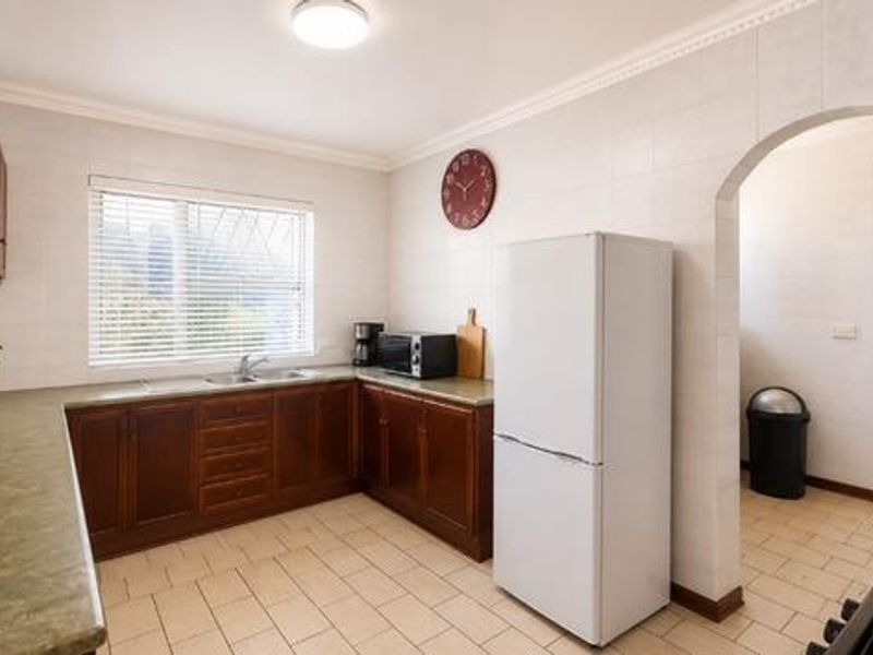 A functional kitchen featuring wooden cabinetry, laminate countertops, tiled flooring, and an arched entryway leading to an adjacent utility space.