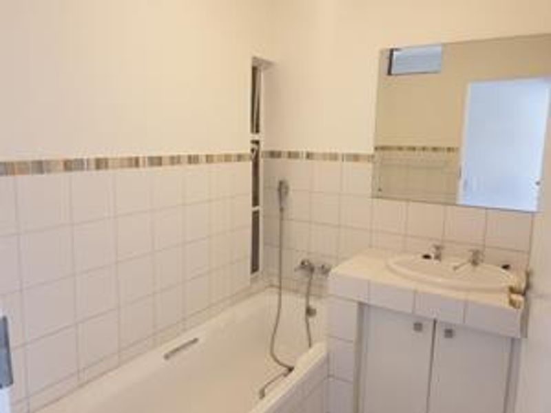 A functional bathroom featuring a built-in bathtub, vanity cabinet with integrated washbasin, and wall-mounted mirror with tiled wall finishes.